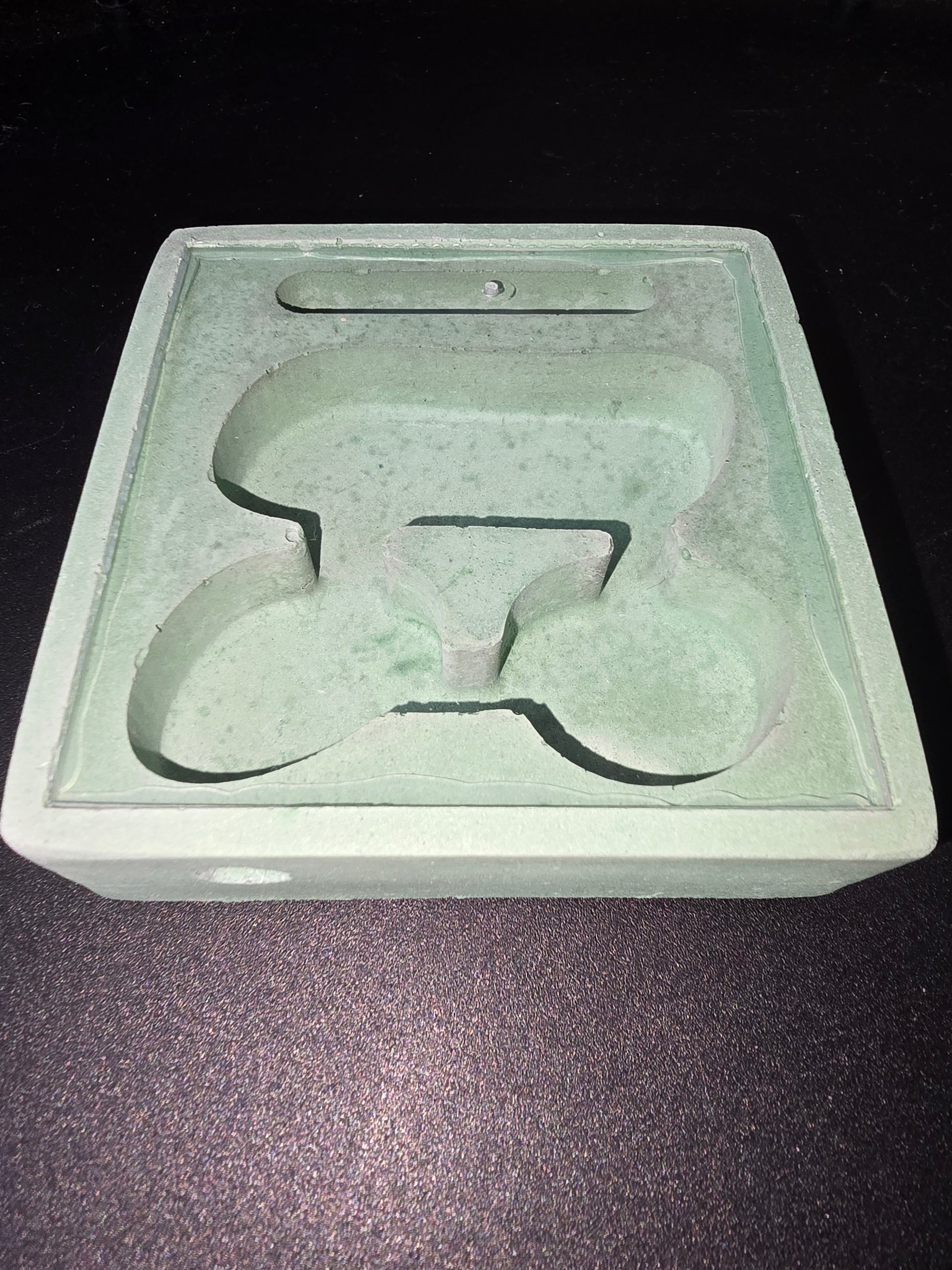 Pièce en plastique vert pâle avec empreinte en forme de logo PETIT gravée, surface poussiéreuse et fissure légère.