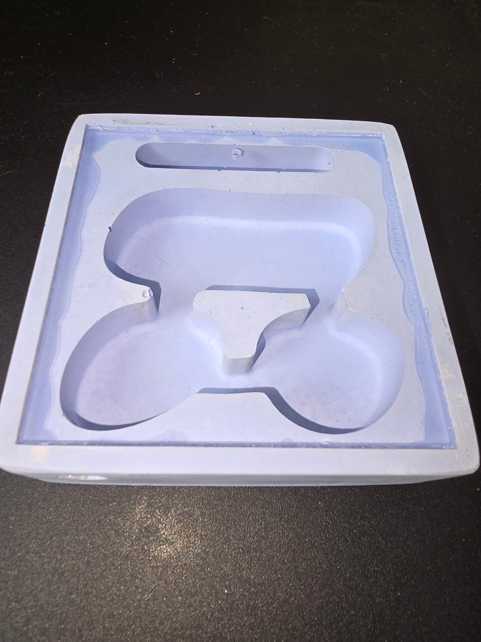 Poêlon en silicone ou moule de cuisson bleu clair avec emporte-pièce en forme de lettre “P” stylisée ou motif abstrait, posé sur une surface sombre.