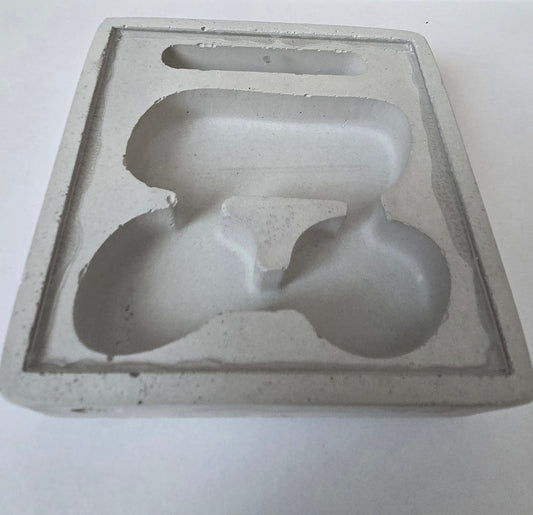 Moule en mousse ou pâtisserie en forme abstraite avec deux lobes ovales reliés, en gris clair, dans un sachet ou cadre plat.